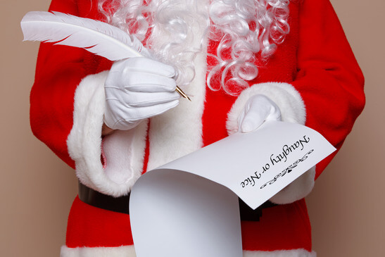 Santa Claus holding a quill pen whilst checking the naughty or nice list.